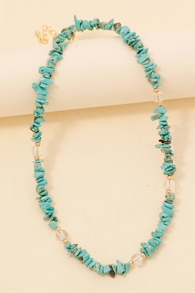 A turquoise pebble stone necklace with gold-colored metal clasp, displayed against a beige background.