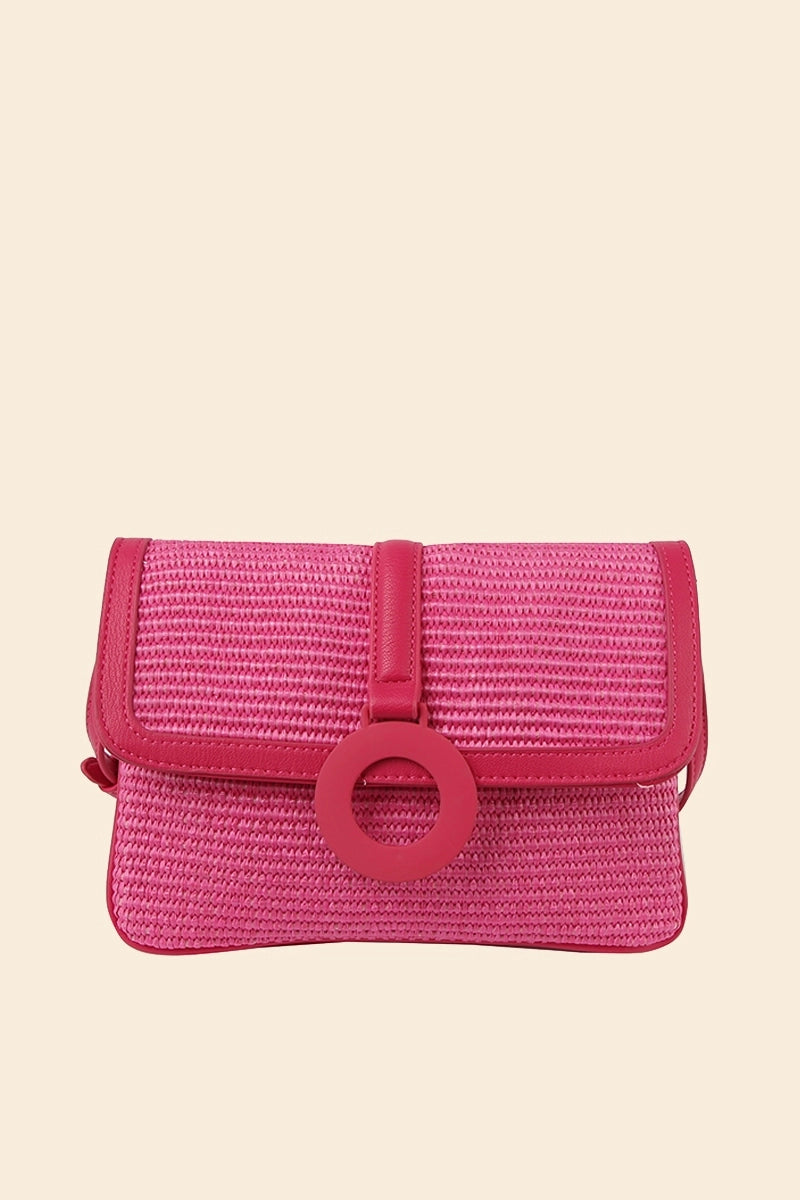 A pink straw crossbody bag with a flap closure and a ring detail on the front.