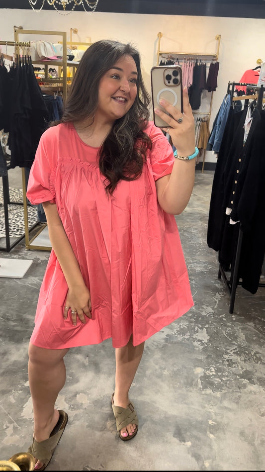 Woman taking a mirror selfie wearing a pink dress in a clothing store.